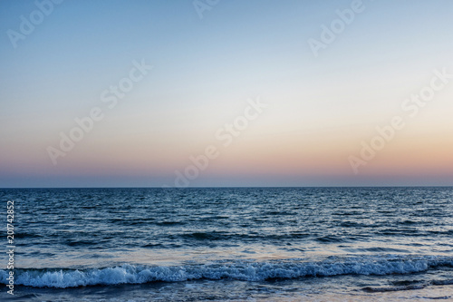 blue sea at sunset. the waves are to the shore. the sun over the horizon
