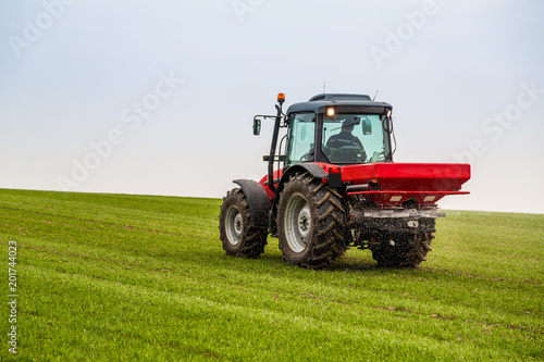 Farmer in tractor fertilizing wheat field at spring with npk