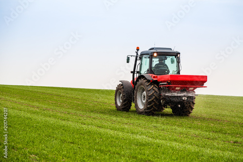 Farmer in tractor fertilizing wheat field at spring with npk