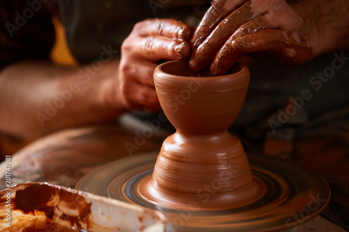 Adult male potter master modeling the clay plate on potter's wheel. Top view, closeup, hands only.