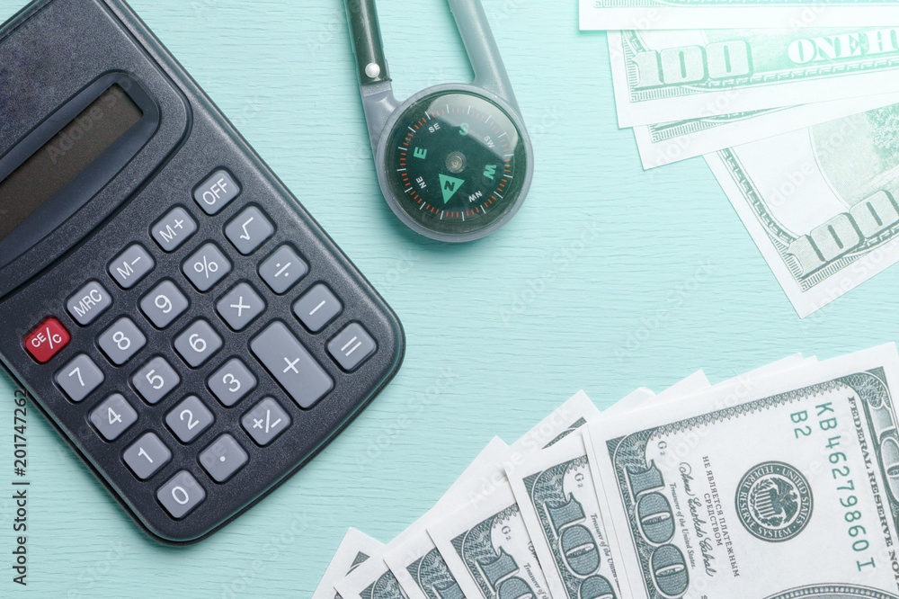 Calculator, a hundred dollar bills and a compass on a blue background, the calculation of funds for the journey Calculator, a hundred dollar bills and a compass on a blue background, the calculation of funds for the journey