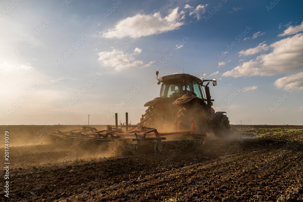 Fototapeta premium Tractor cultivating field at spring