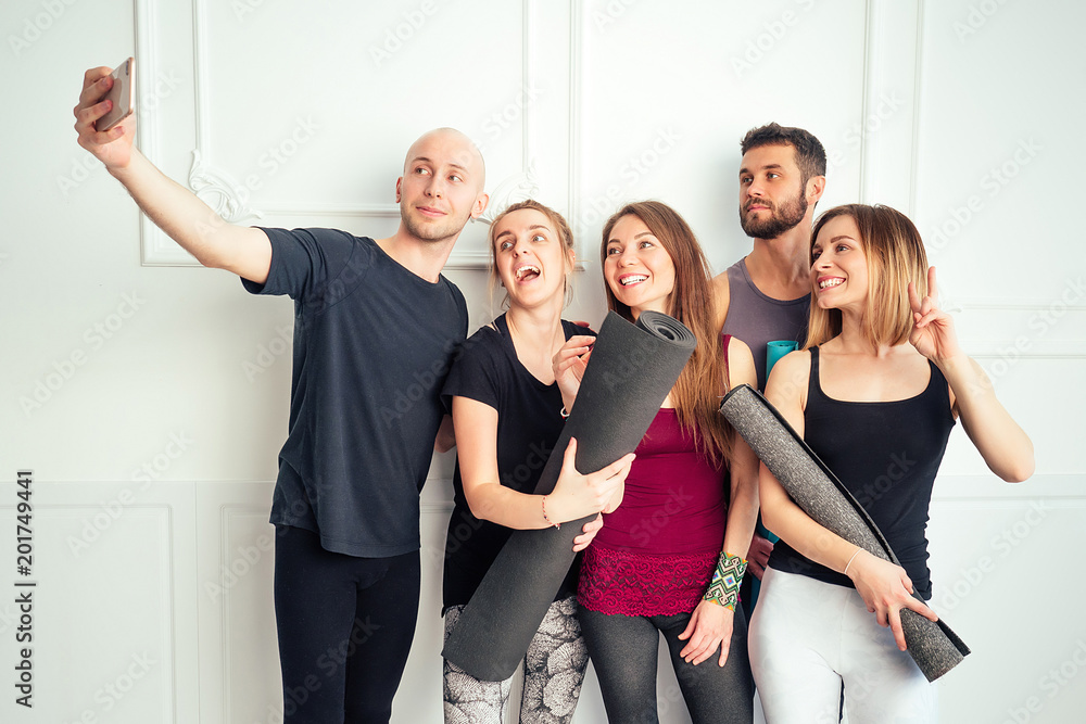 Fototapeta premium a happy group of people from man and woman practicing yoga in the studio and making selfies on the phone. groups of meditation and support in the yoga class. men and women have fun
