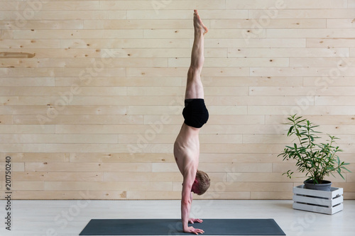 Fototapeta Sporty man practices yoga handstand asana Adho Mukha Vrikshasana at the yoga studio