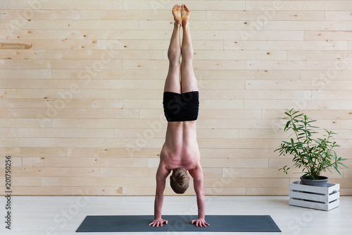 Sporty man practices yoga handstand asana Adho Mukha Vrikshasana at the yoga studio. Balance exercise