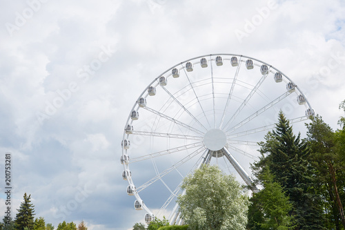 Ferris wheel in contemporary amusement park among green and blooming trees and grey cloudy sky © pressmaster
