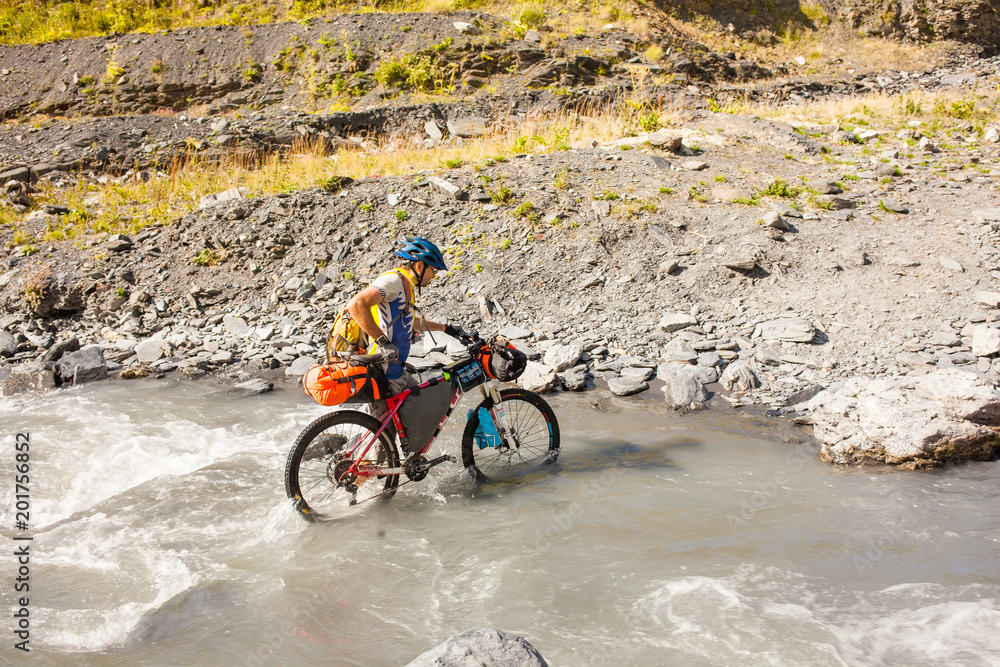 Mountain biker is crossing the river in the highlands of Tusheti region, Georgia Mountain biker is crossing the river in the highlands of Tusheti region, Georgia
