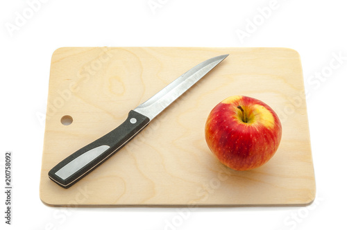 Ripe red juicy apple and knife on a cutting board made of light wood.