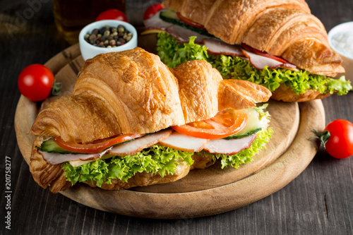 Fresh croissant or sandwich with salad, ham, jamon, prosciutto, salami, cheese, chicken, tomatoes on wooden background. Morning breakfast concept. Healthy and fast food.