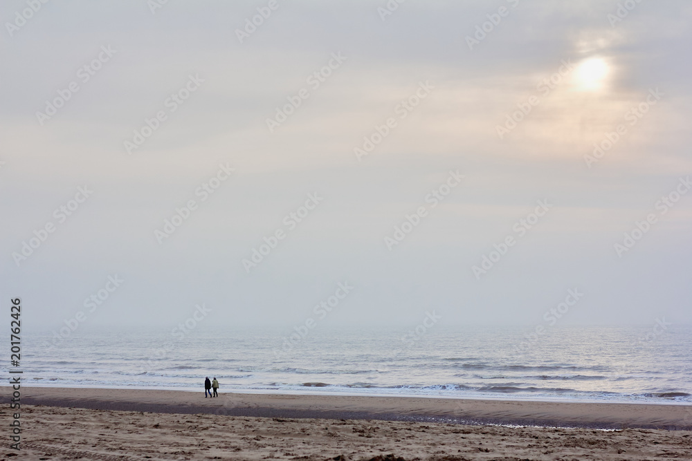 Lonely silhouettes of two people walking along the cold winter shore of the north sea at sunset