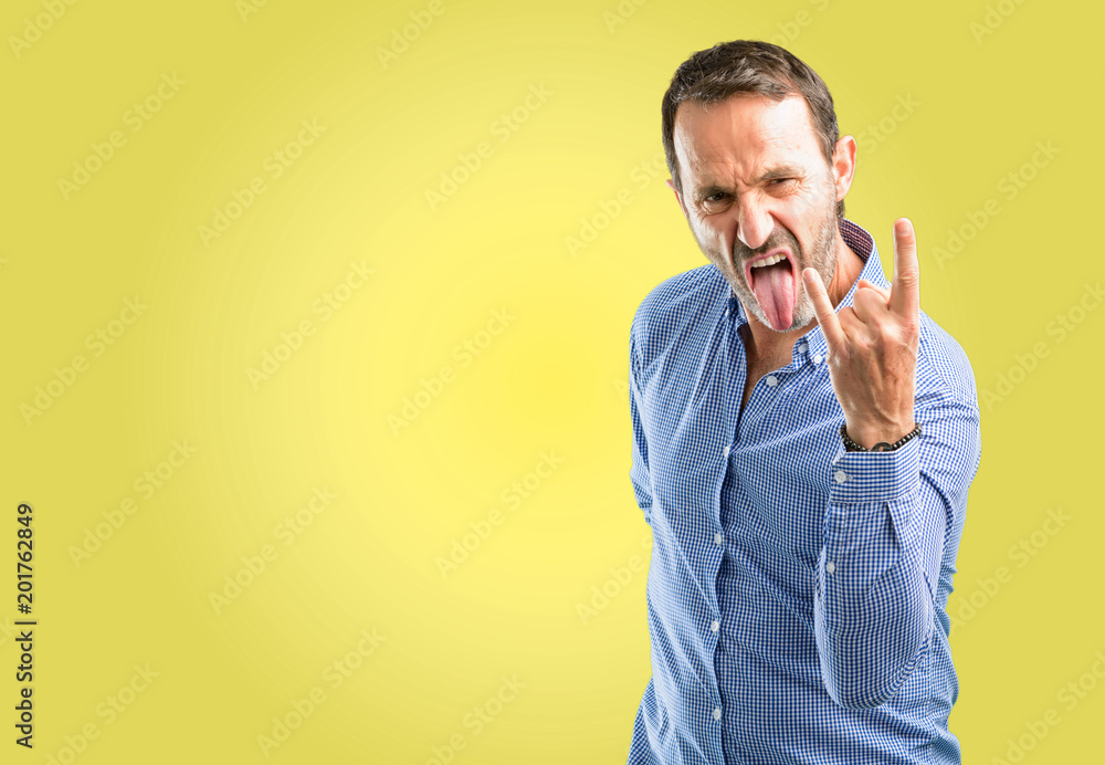 Handsome middle age man making rock symbol with hands, shouting and celebrating with tongue out Handsome middle age man making rock symbol with hands, shouting and celebrating with tongue out