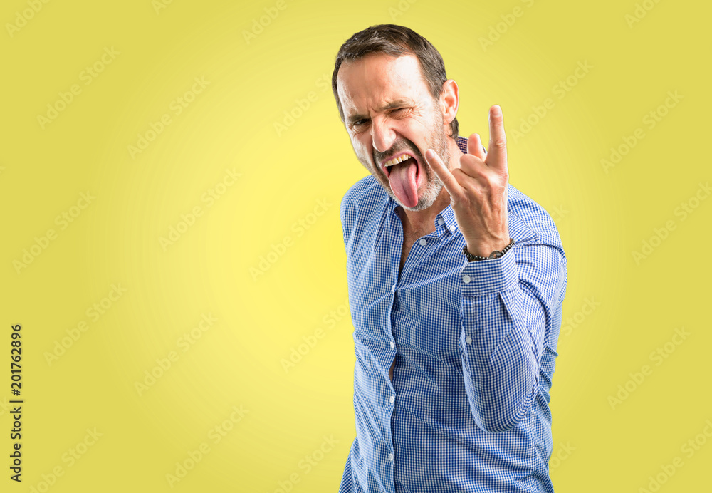 Handsome middle age man making rock symbol with hands, shouting and celebrating with tongue out Handsome middle age man making rock symbol with hands, shouting and celebrating with tongue out