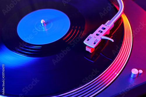 Turntable vinyl record player on the background of a sunset over the lights city. Sound technology for DJ to mix & play music. Black vinyl record. Needle on a vinyl record