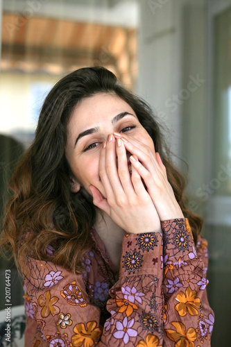 Woman portrait; smily woman is covering her mouth with hands.