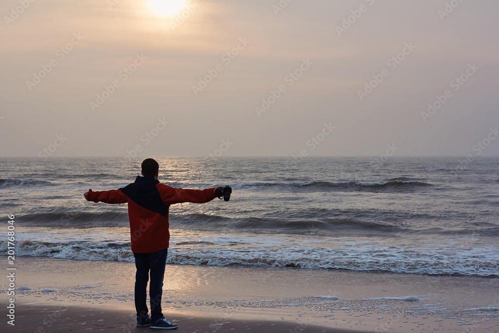Young man stands on the shore of the North sea with outstretched arms and looks into the distance