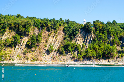Scenic green island with a small white lighthouse near the sea with fish net and a boat