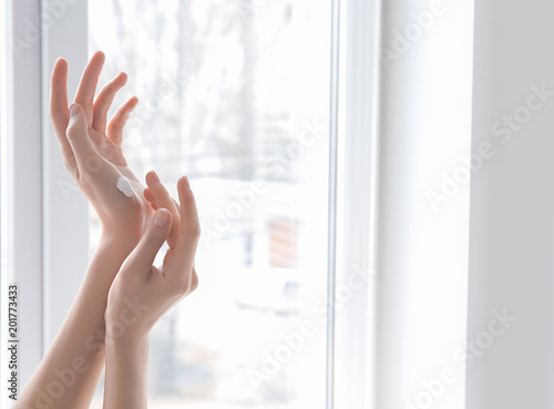Young woman applying hand cream against window