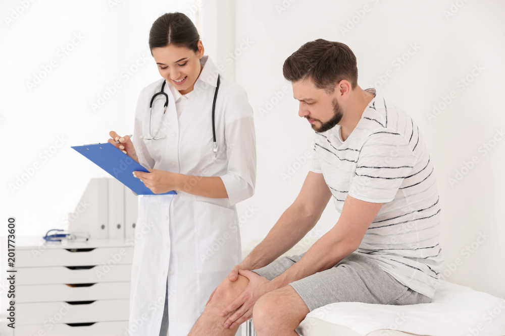 Doctor examining male patient with injured leg in clinic Doctor examining male patient with injured leg in clinic