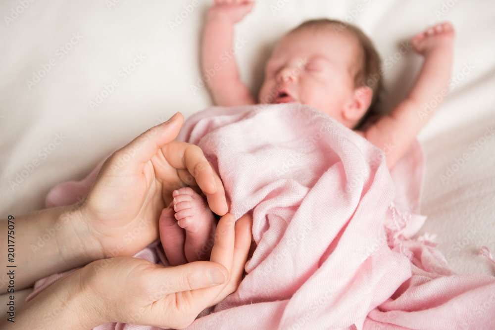 Mom's hands hold the legs of a newborn baby Mom's hands hold the legs of a newborn baby