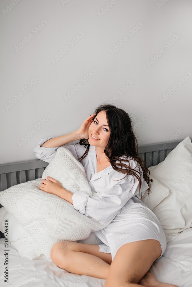 sexy young brunette woman wearing a white shirt on the bed at home. Girl's morning sexy young brunette woman wearing a white shirt on the bed at home. Girl's morning