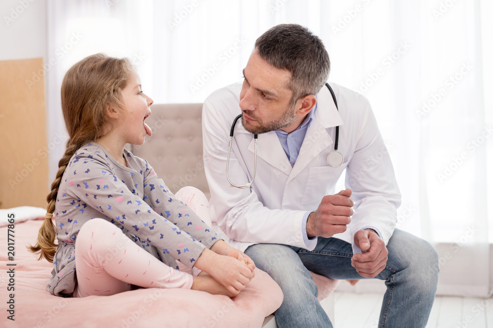 Usual checkup. Serious professional doctor examining a little girl and she showing her throat Usual checkup. Serious professional doctor examining a little girl and she showing her throat