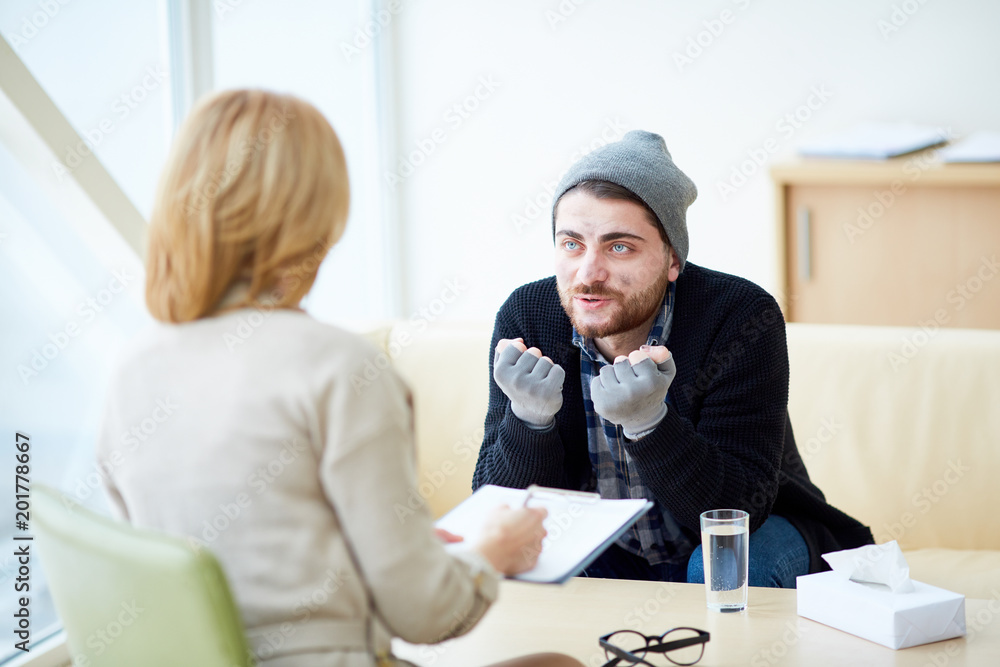 Young refugee in need explaining his problems to psychologist during session in social support center Young refugee in need explaining his problems to psychologist during session in social support center