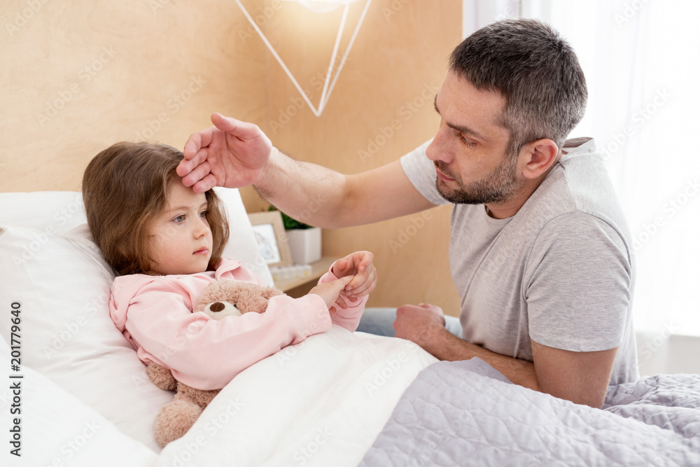 I adore you. Loving devoted daddy touching his girls forehead and the girl lying in bed