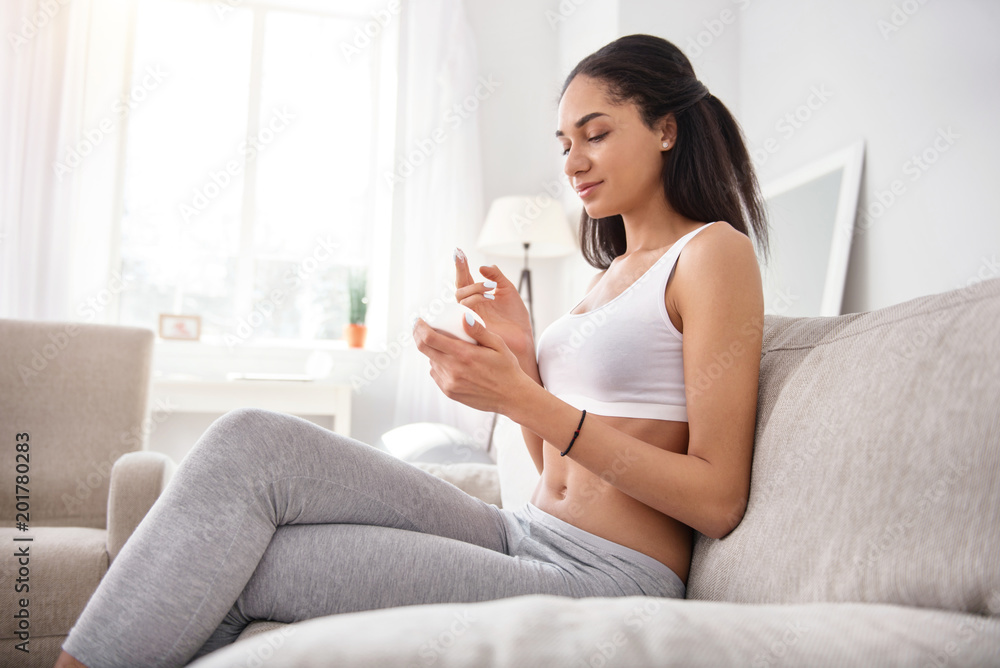 High-quality product. Beautiful young woman sitting on the sofa and being about to apply some cream to her face while looking inside the jar High-quality product. Beautiful young woman sitting on the sofa and being about to apply some cream to her face while looking inside the jar