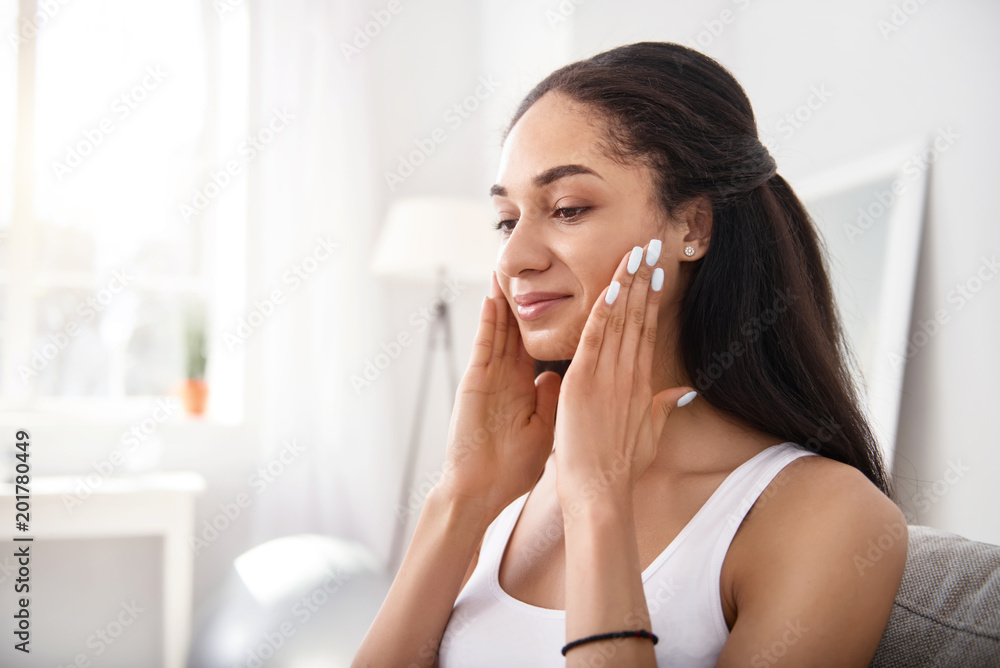 Anti-ageing massage. Beautiful dark-haired young woman rubbing her cheeks with her fingers while doing a facial massage Anti-ageing massage. Beautiful dark-haired young woman rubbing her cheeks with her fingers while doing a facial massage