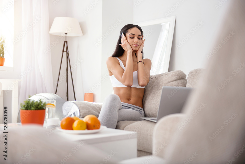 Enjoyable treatment. Athletic young woman cupping her face with both hands and doing a massage while watching a video tutorial online on laptop Enjoyable treatment. Athletic young woman cupping her face with both hands and doing a massage while watching a video tutorial online on laptop