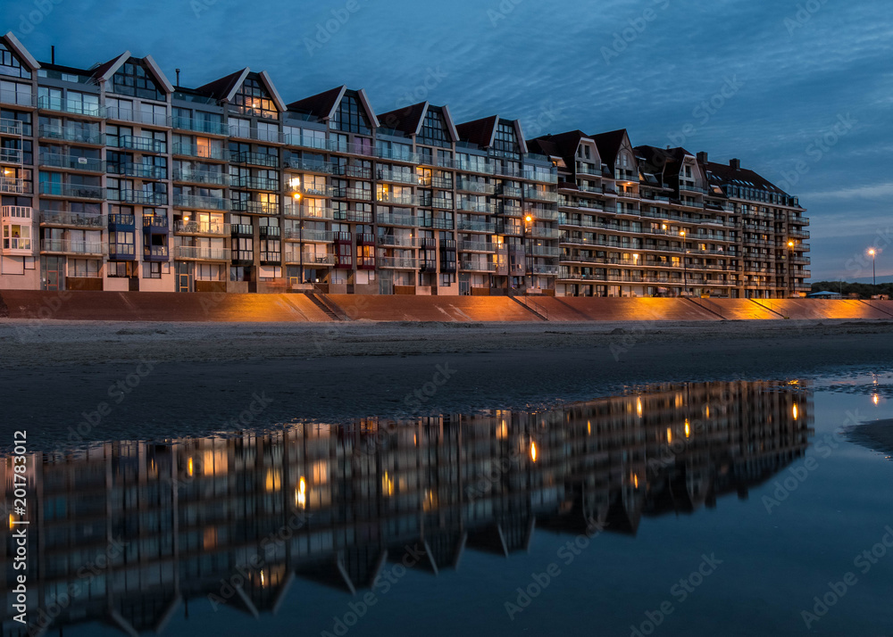 Glass front of building at the beach mirrors in water after sunset