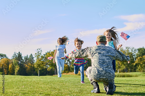 Soldier is meeting his family outdoors. Happy reunion of father and kids on the grass.