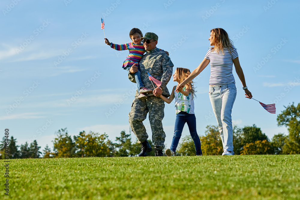 Soldier with his family are walking with usa flags. Father came back grou US army and wealking with his daughters and wife on the grass. Soldier with his family are walking with usa flags. Father came back grou US army and wealking with his daughters and wife on the grass.