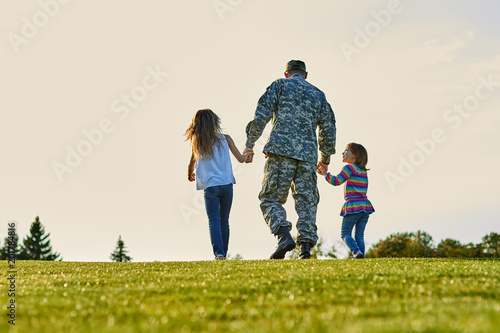 Soldier walking with little girls holding hands. Back view, father and daughters are walking together.