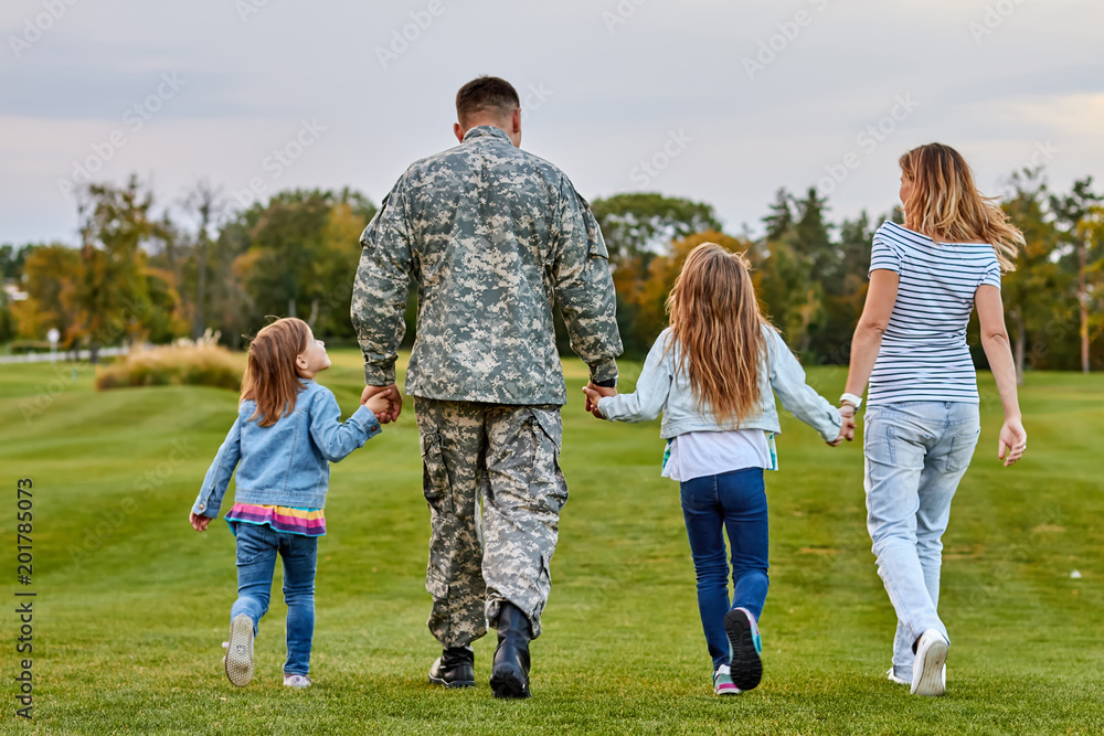 Back view soldier's family walking. Soldier at vacation. Four family members walking together holding hands. Back view soldier's family walking. Soldier at vacation. Four family members walking together holding hands.