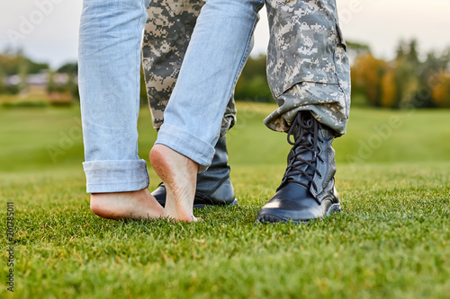Close up soldier boots and girlfriend with naked feet. Standing on the grass. © DenisProduction.com
