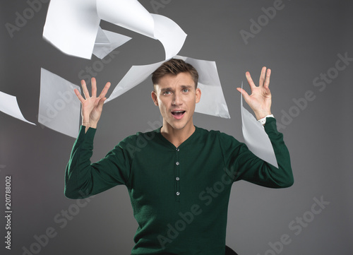 Waist up portrait of screaming man sitting and throwing up papers. He is looking at camera with anger. Isolated on background