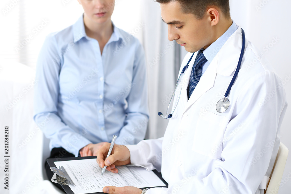 Male doctor holding application form while consulting female patient in hospital office. Perfect service in medicine and healthcare concept Male doctor holding application form while consulting female patient in hospital office. Perfect service in medicine and healthcare concept