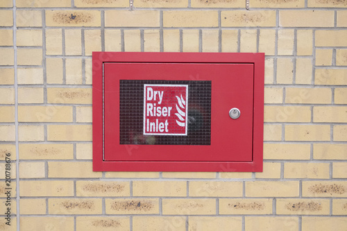Dry riser inlet box red on brick wall for emergency fire services water connection for hose brigade engine at shopping mall retail park