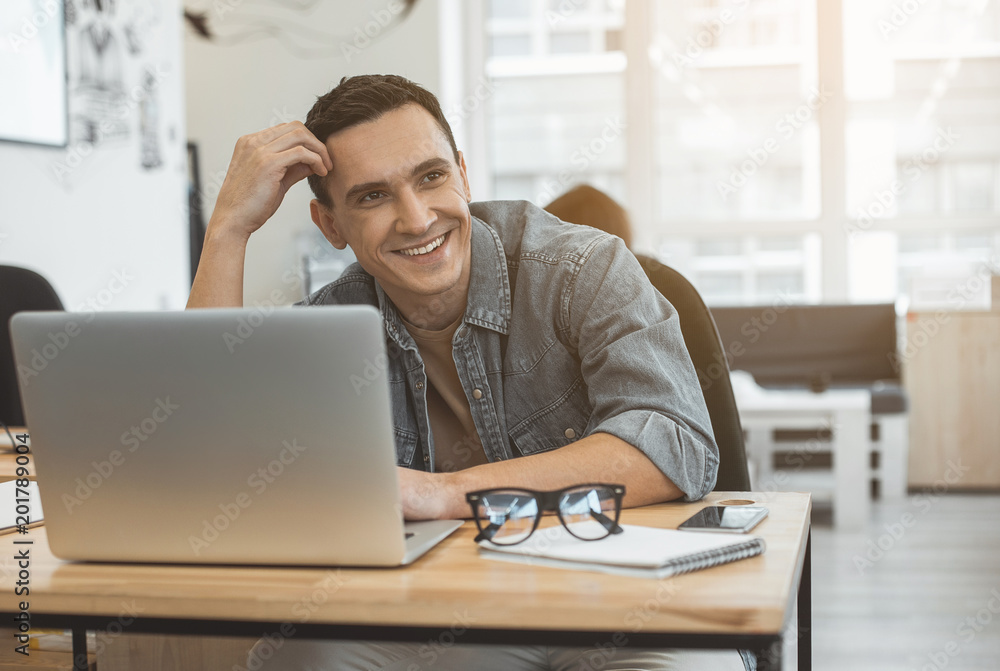 Portrait of cheerful man typing in laptop while sitting at desk in office. Beaming employee at job concept Portrait of cheerful man typing in laptop while sitting at desk in office. Beaming employee at job concept