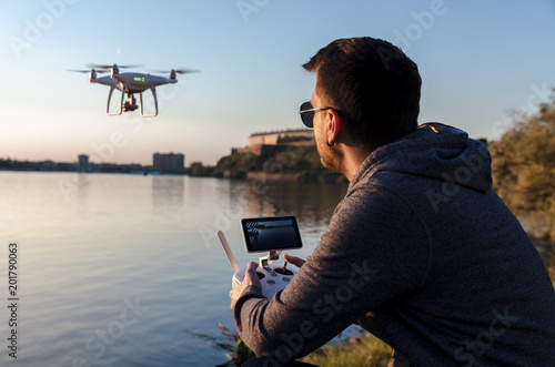 Man operating / flying with drone by the river at sunset , closeup and back view shot 