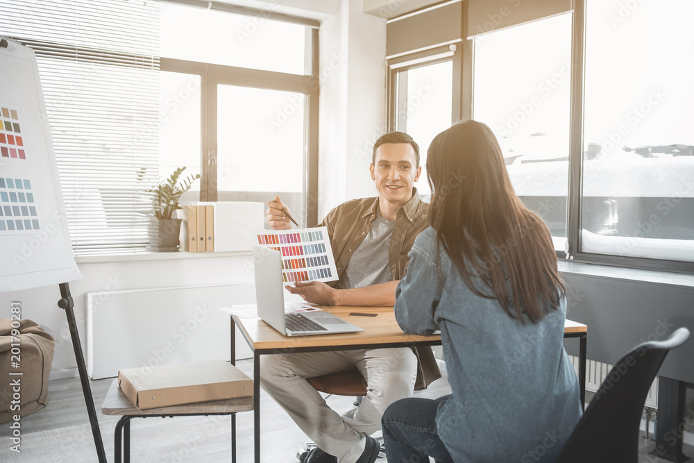 Portrait of beaming stylist of interior proposing different colors for walls. He talking with female client at desk. Creative occupation concept Portrait of beaming stylist of interior proposing different colors for walls. He talking with female client at desk. Creative occupation concept