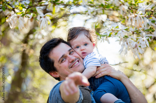 Young father with child have a leisure in springtime flowering garden in sunny day.