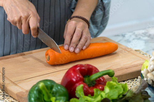 Close-up of hand woman carrot with kitchen knife on cutting board. Chef cuts the vegetables into a meal.