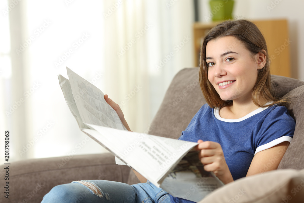 Teen reading a newspaper looking at camera at home Teen reading a newspaper looking at camera at home