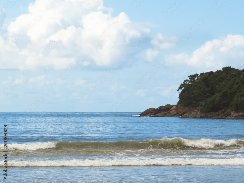 Fototapeta premium Waves on the beach with island to the background in sky with clouds.