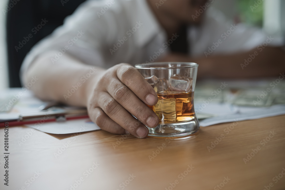 Close up. Hand of asian businessman holding a glass of whiskey. he feel stressed, disappoint during working. alcohol addiction - drunk businessman concept
