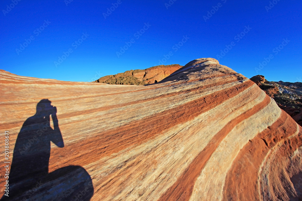 Photographer sitting on the Fire Wave rock at sunset, Valley of Fire State Park, Nevada, USA