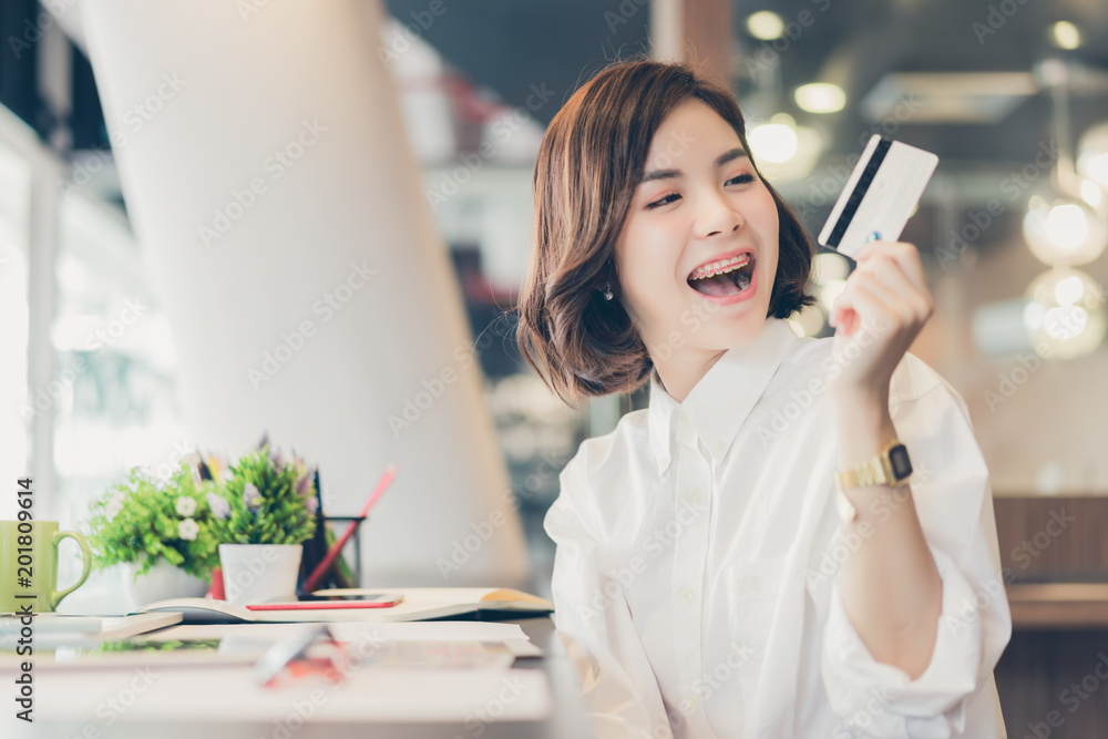 Obraz premium Young beautiful asian woman working on desk with tablet and showing credit card in coworking spaces.