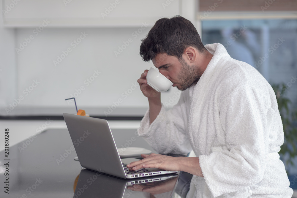 A man in a robe with a laptop at home A man in a robe with a laptop at home